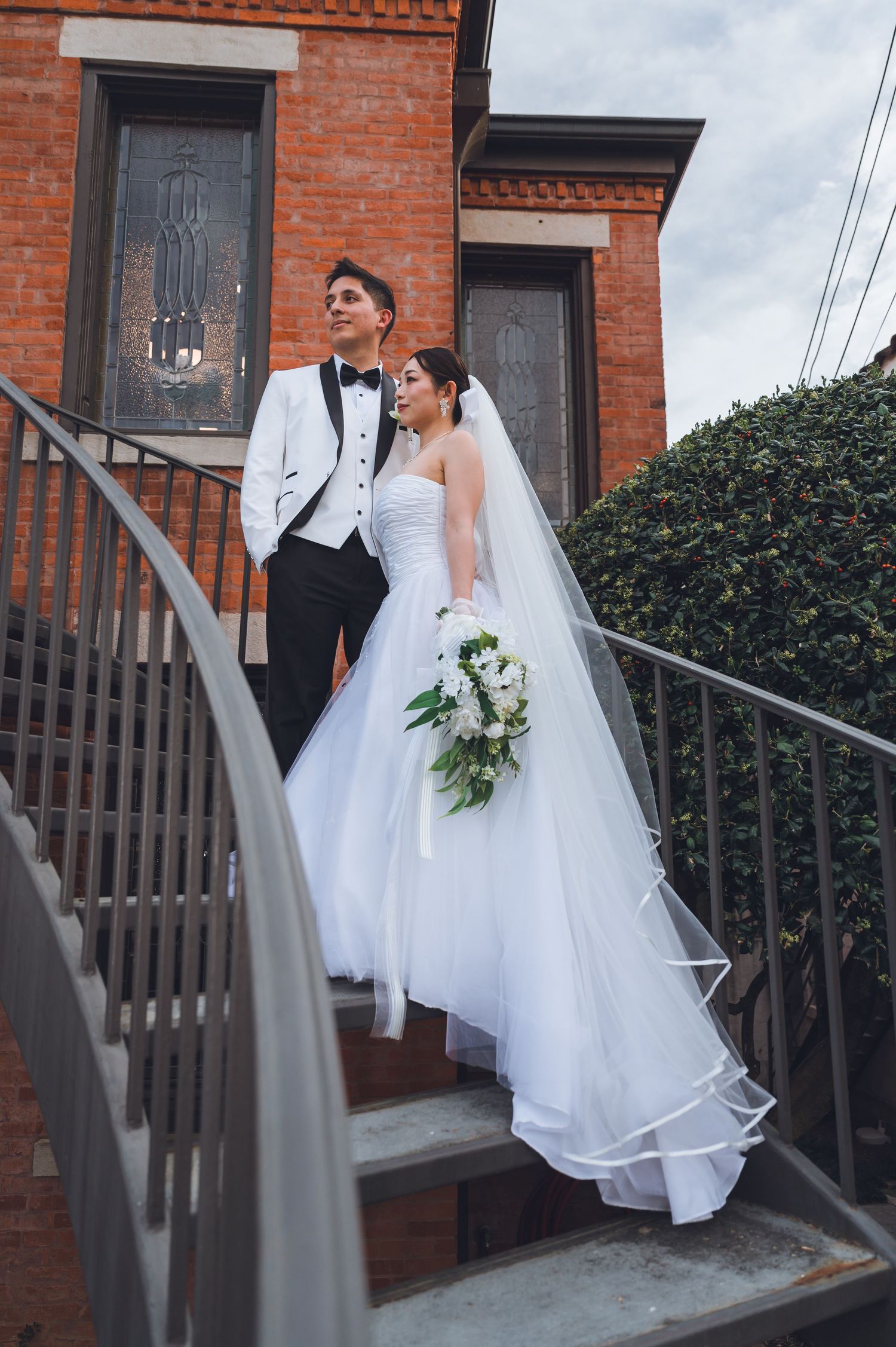 Bride and groom standing on stairs outside brick building on their wedding day.