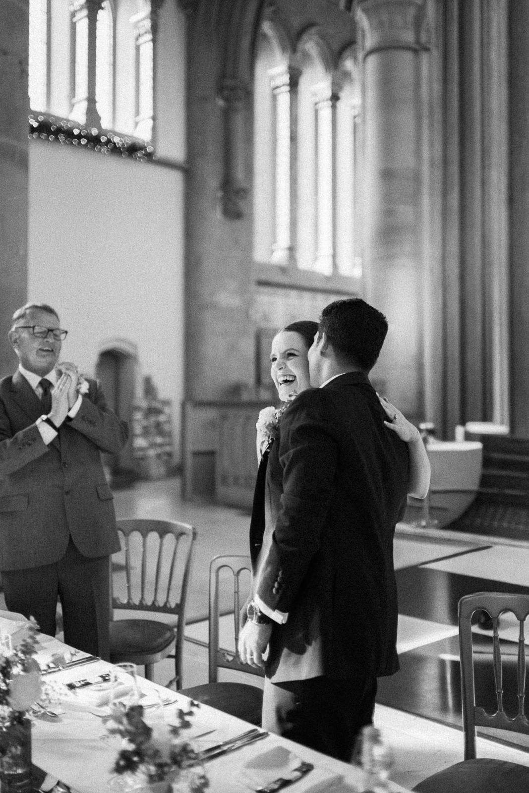 Black and white photo of blurred wedding guests moving through a Gothic church with arched columns and stained glass windows.