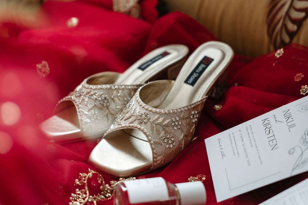 Elegant embellished bridal heels with floral beading on red fabric beside nail polish and wedding stationery.