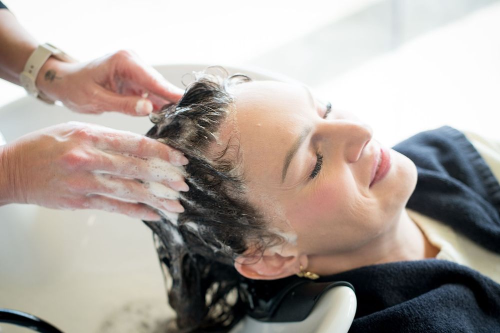 Woman getting a relaxing hair wash at a salon, with hands massaging shampoo into her wet hair.