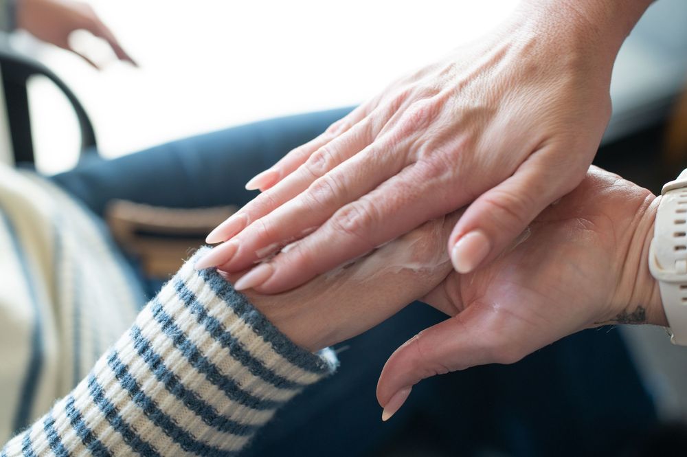 A younger hand gently rests on an elderly person's hand, symbolizing care, support, and compassion.