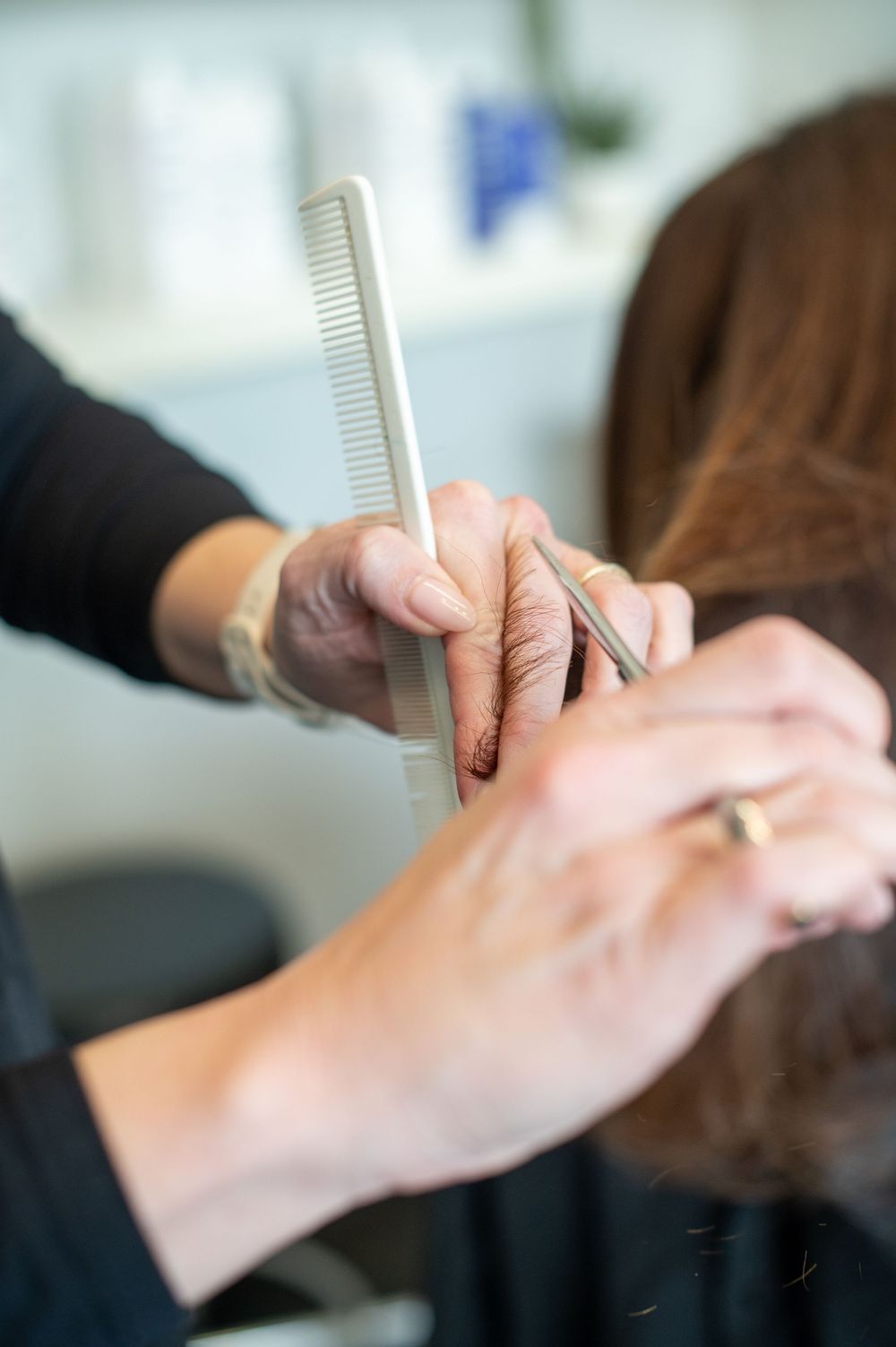 Hairdresser cutting brown hair with scissors and comb in a professional salon setting.