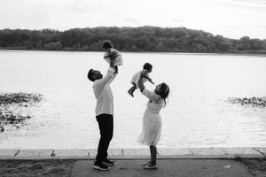 A mother and father both lift their twin daughters in the air above their head near a lake