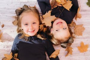 An aerial shot of two sisters laying down with their heads together and Autumn leaves surrounding them