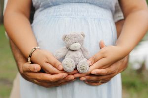 A photo of a mother’s belly while holding a small teddy near for her baby