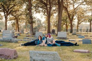 Family of four sits together among gravestones under tall trees in a historic cemetery during an autumn photo session.