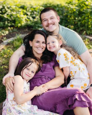 A family of 4 huddle together and smile at the camera