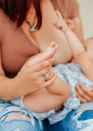 A photo of a mother holding her daughter’s foot while nursing