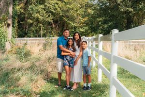 A  photo of a family of four standing by a fence on a sunny day