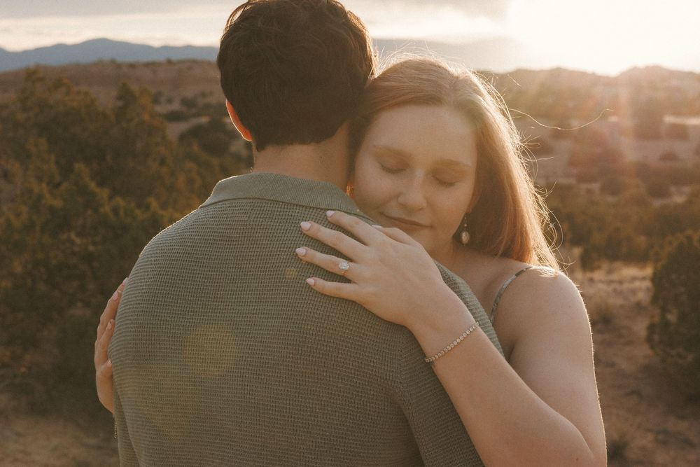 Couple embracing at golden hour with desert landscape and mountains in the background.