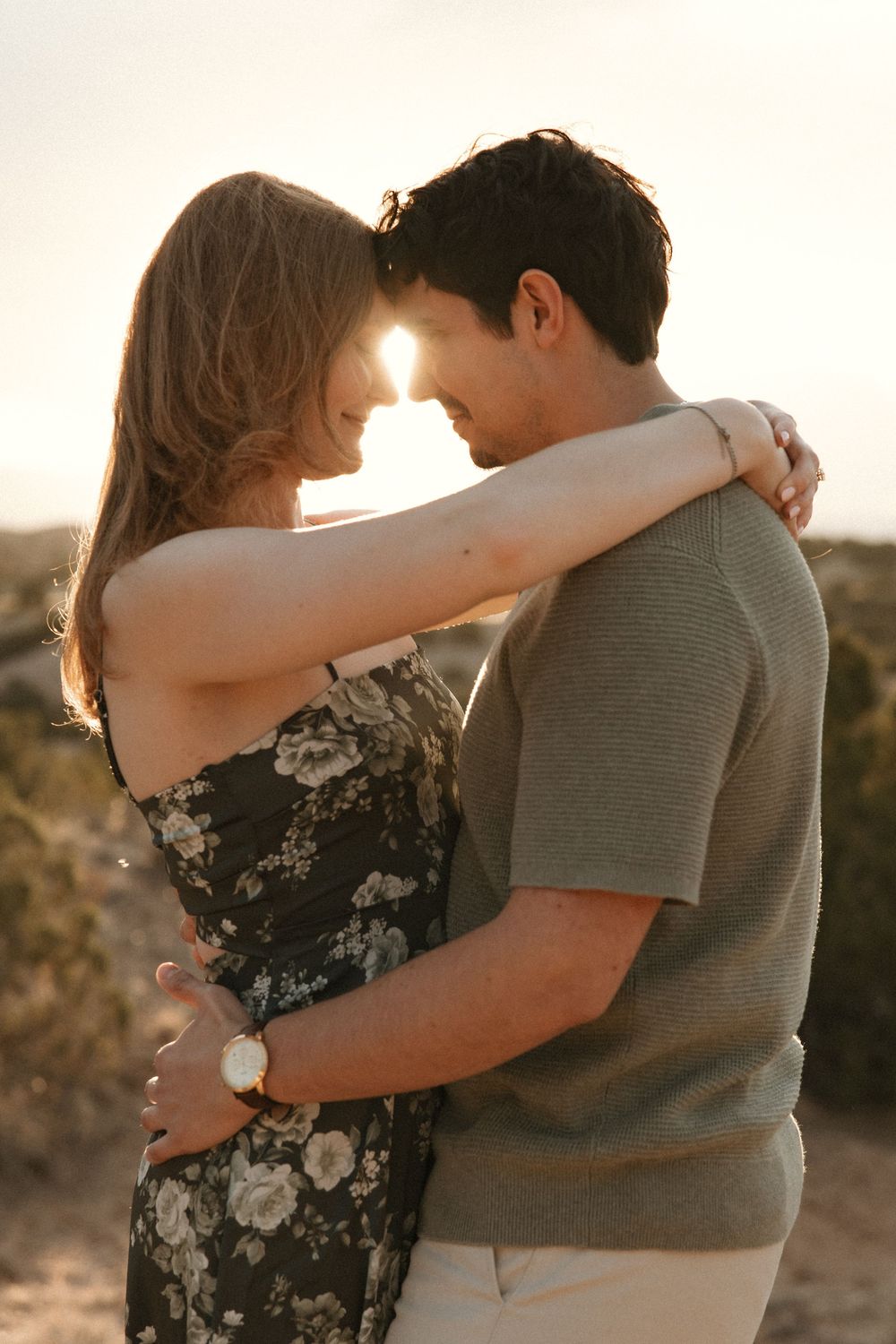Couple sharing an intimate moment backlit by a warm sunset in a desert setting, woman in floral dress.