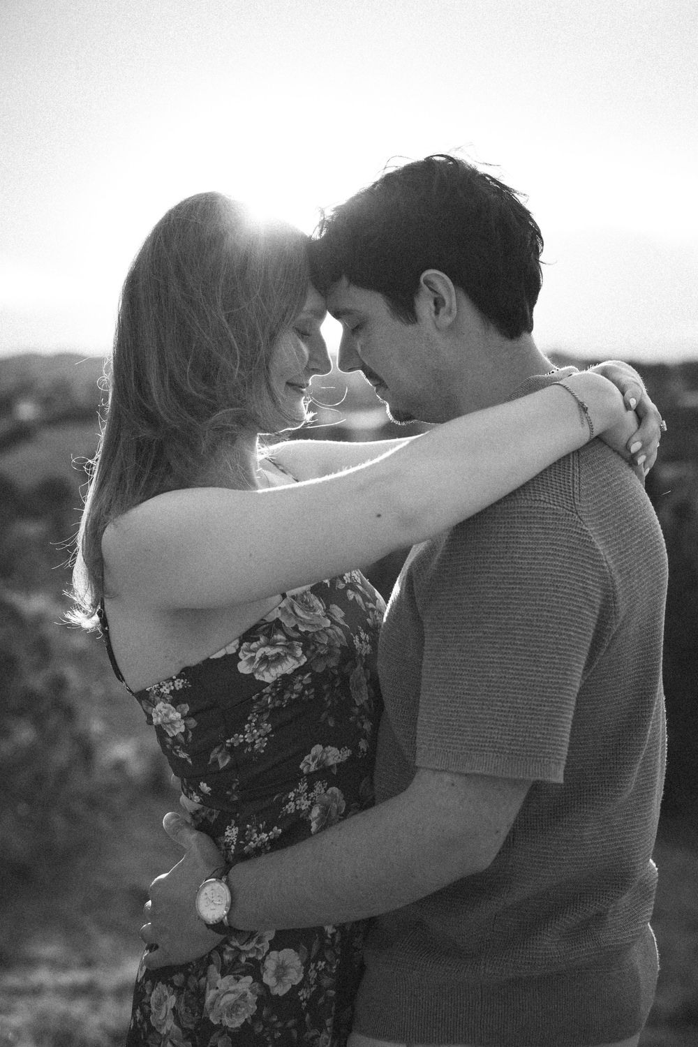 Black and white photo of a couple embracing forehead to forehead at sunset in a desert landscape.