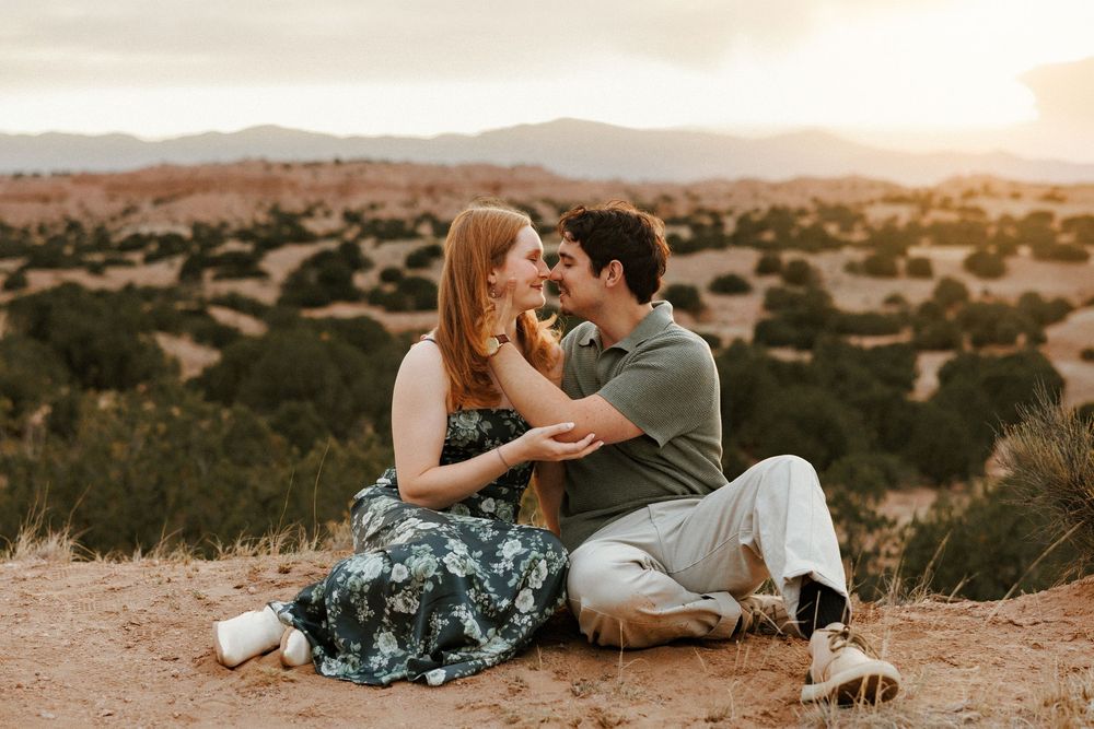 Couple sitting together on desert ground at golden hour with mountain landscape backdrop.