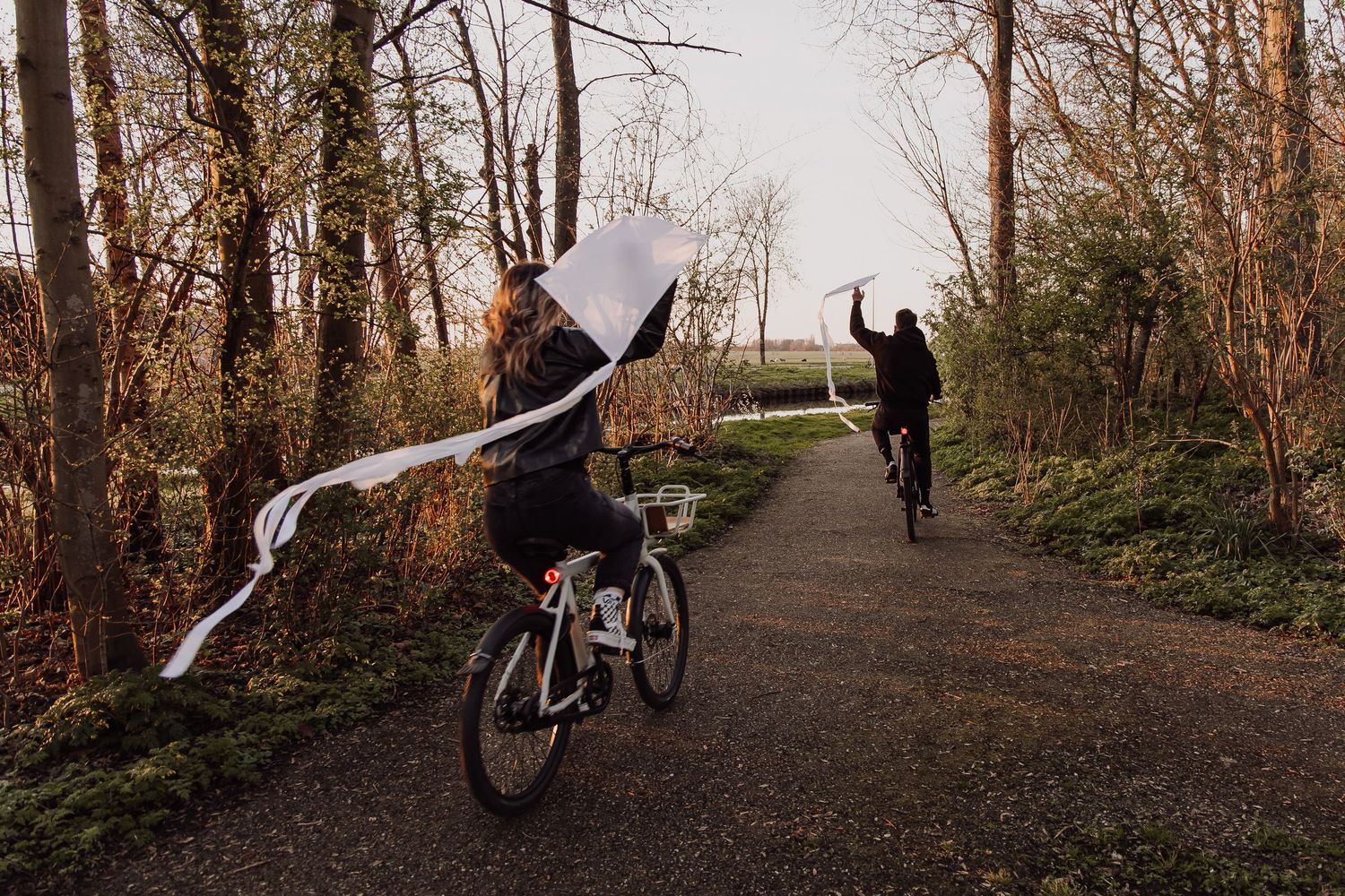 Couple cycling together at sunset while holding white kites during a romantic outdoor photoshoot.