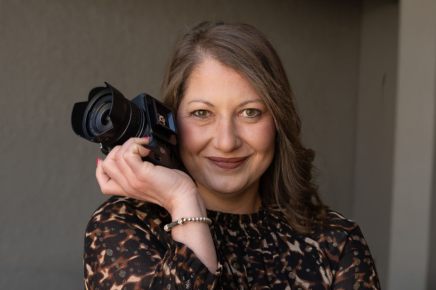 Professional female photographer smiling while holding a DSLR camera outdoors.