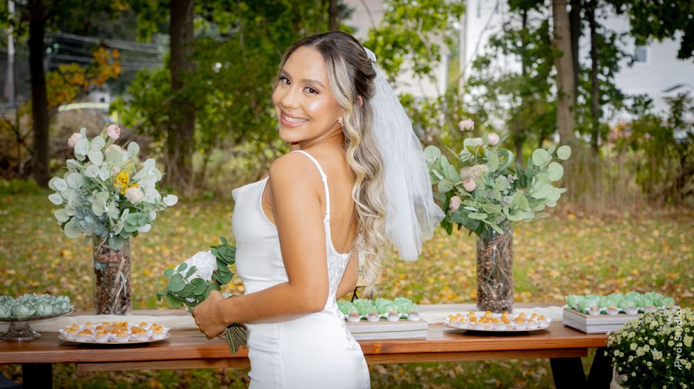 A bride in a white dress and veil smiles over her shoulder at an outdoor fall wedding reception table.