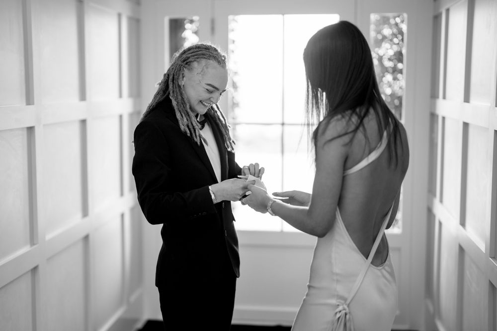 Black and white photo of two people exchanging rings in a doorway during an intimate wedding ceremony.