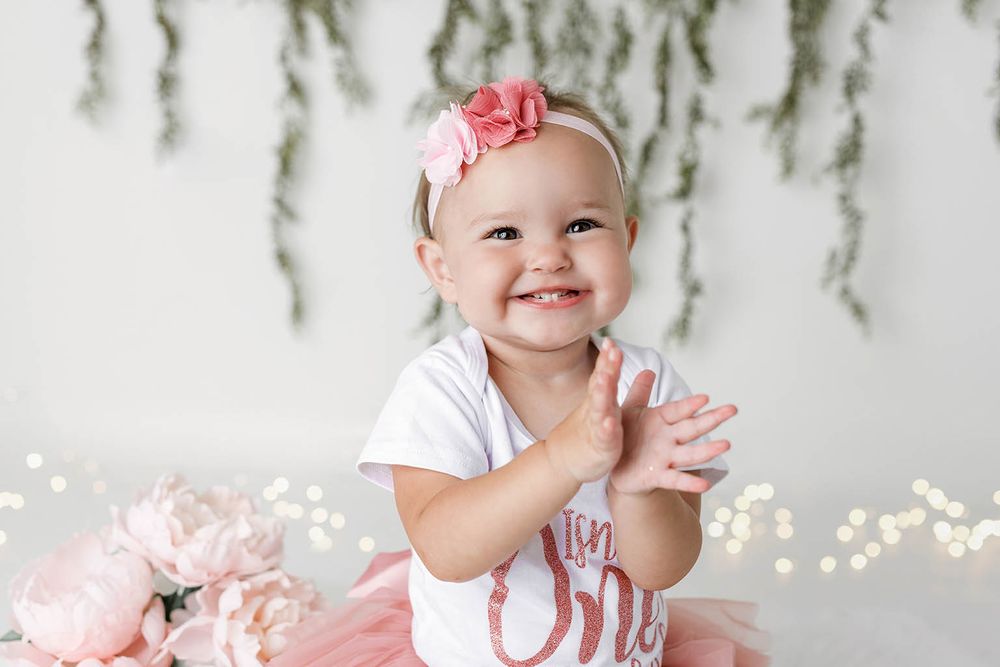 Smiling baby girl in pink tutu claps hands during first birthday photoshoot by Temescal Valley cake smash photographer.