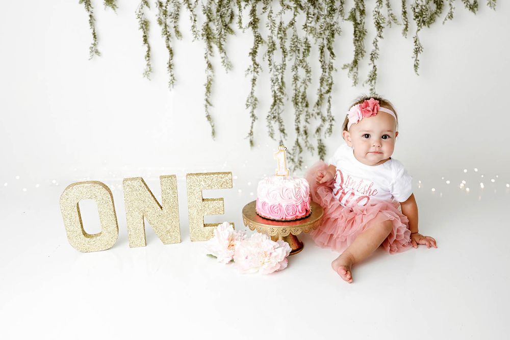 Baby girl in pink tutu celebrates first birthday with cake smash next to glittery ONE letters by Temescal Valley cake smash photographer.