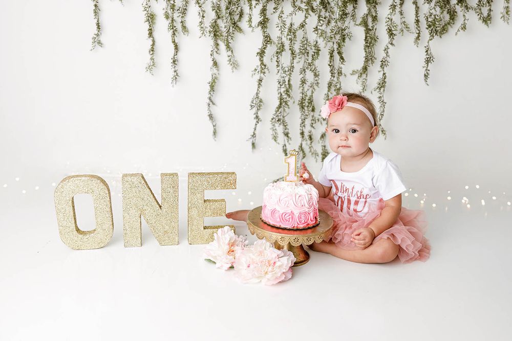 Baby girl in pink tutu celebrates first birthday with cake smash next to glitter ONE sign by Temescal Valley cake smash photographer.