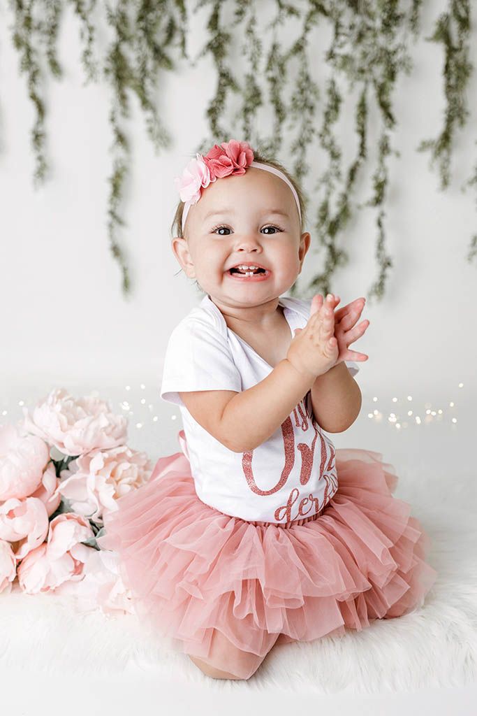 Happy baby girl in ruffled pink tutu laughs and claps during first birthday milestone photoshoot.