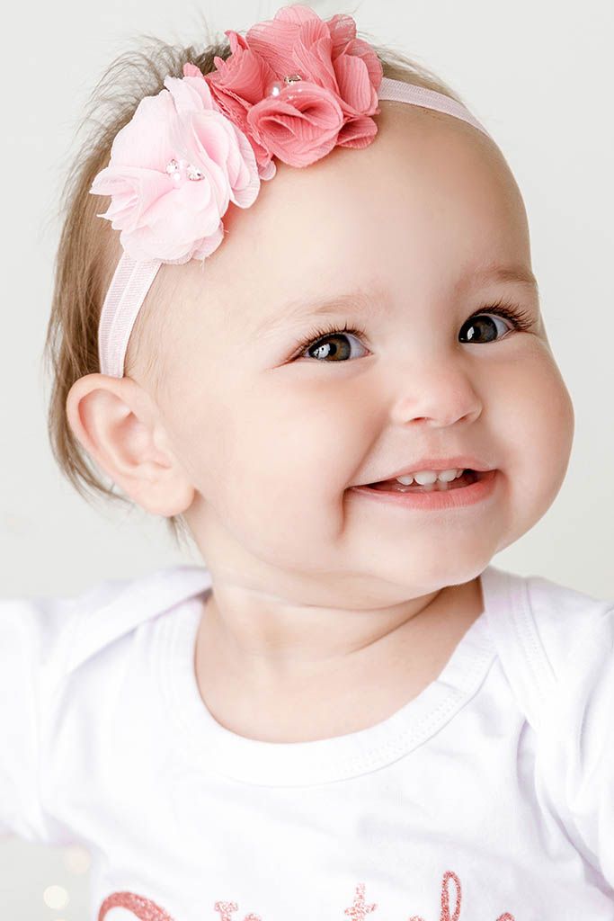 Close-up portrait of happy baby girl smiling with pink floral headband and bright eyes by Temescal Valley cake smash photographer.