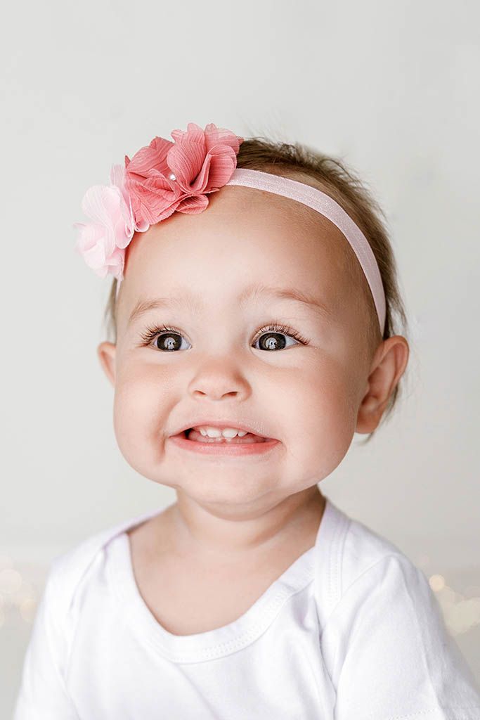 Cute baby girl with pink flower headband smiling sweetly in white outfit portrait by Temescal Valley cake smash photographer.
