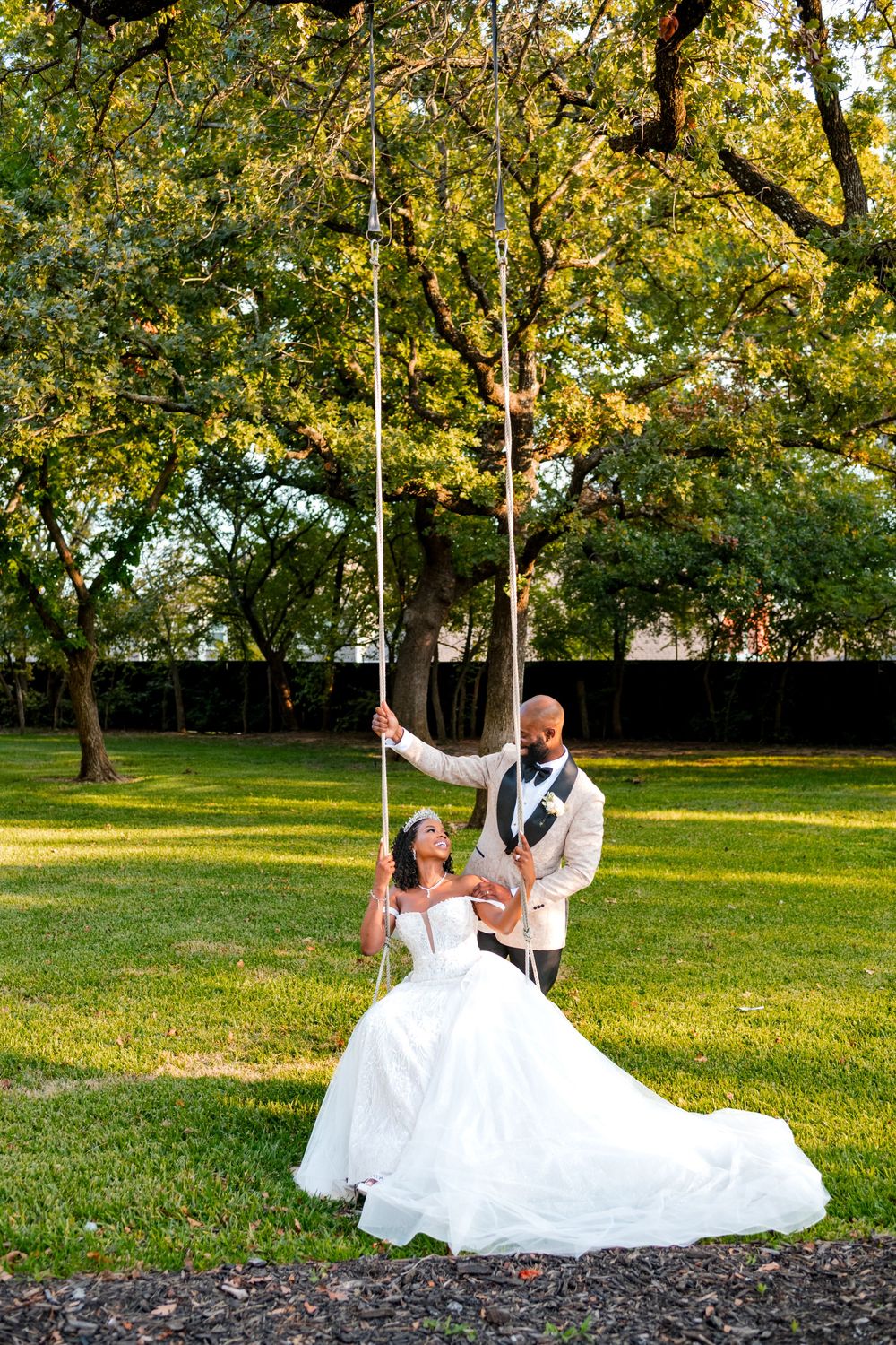 A couple shares a playful moment on a tree swing in a scenic park during their wedding photoshoot.