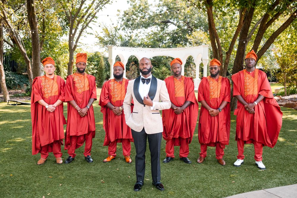 Wedding party members in vibrant red outfits stand together with two people in light-colored suits in a park.