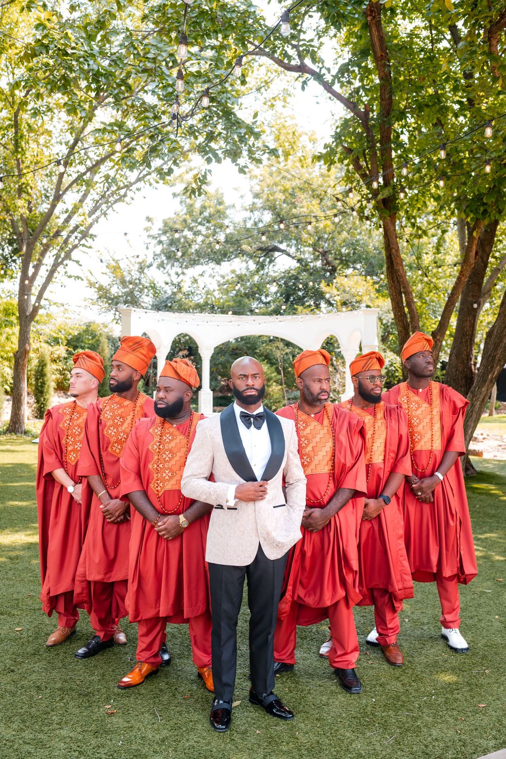 Wedding party poses outdoors in bright red attire and formal wear on a grassy lawn.