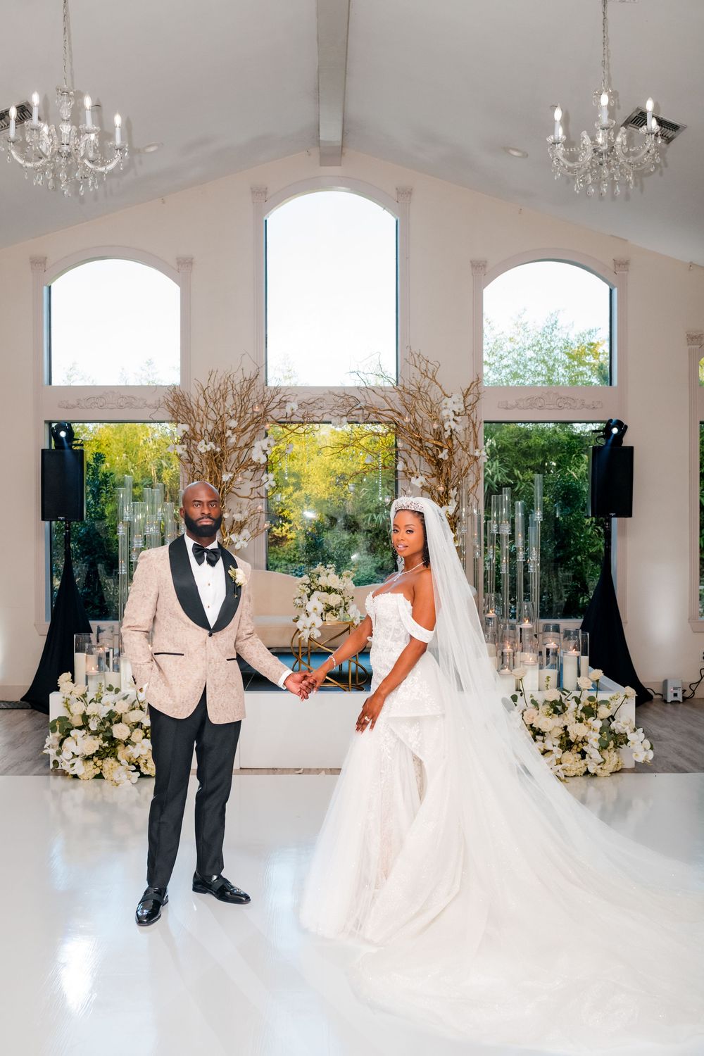 Elegant wedding ceremony setup in a bright chapel with arched windows, chandeliers and floral arrangements.