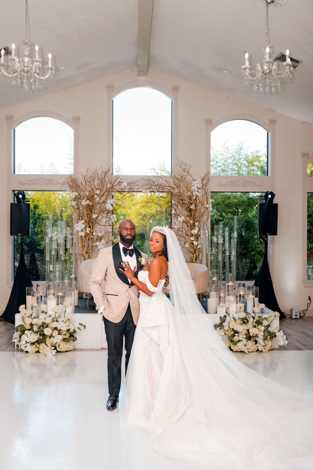Romantic wedding portrait in an elegant white chapel with chandeliers and floral decor.
