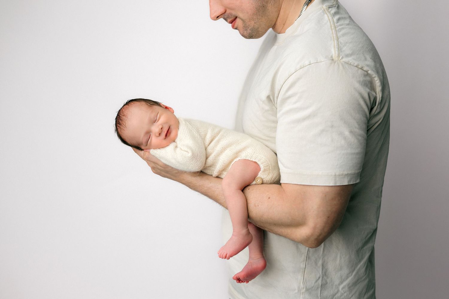 A mother gently holds her newborn baby's tiny hand, wearing a bracelet, against a soft white background.