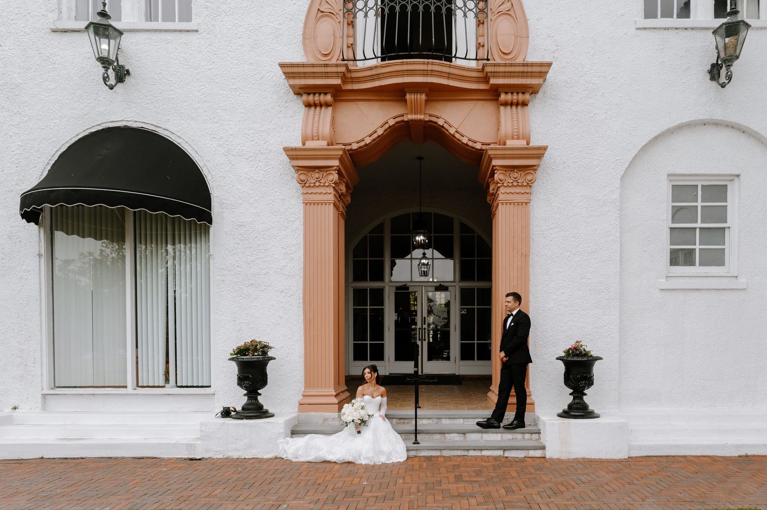 Bride and groom posing outside elegant white venue with ornate pink archway entrance on their wedding day.