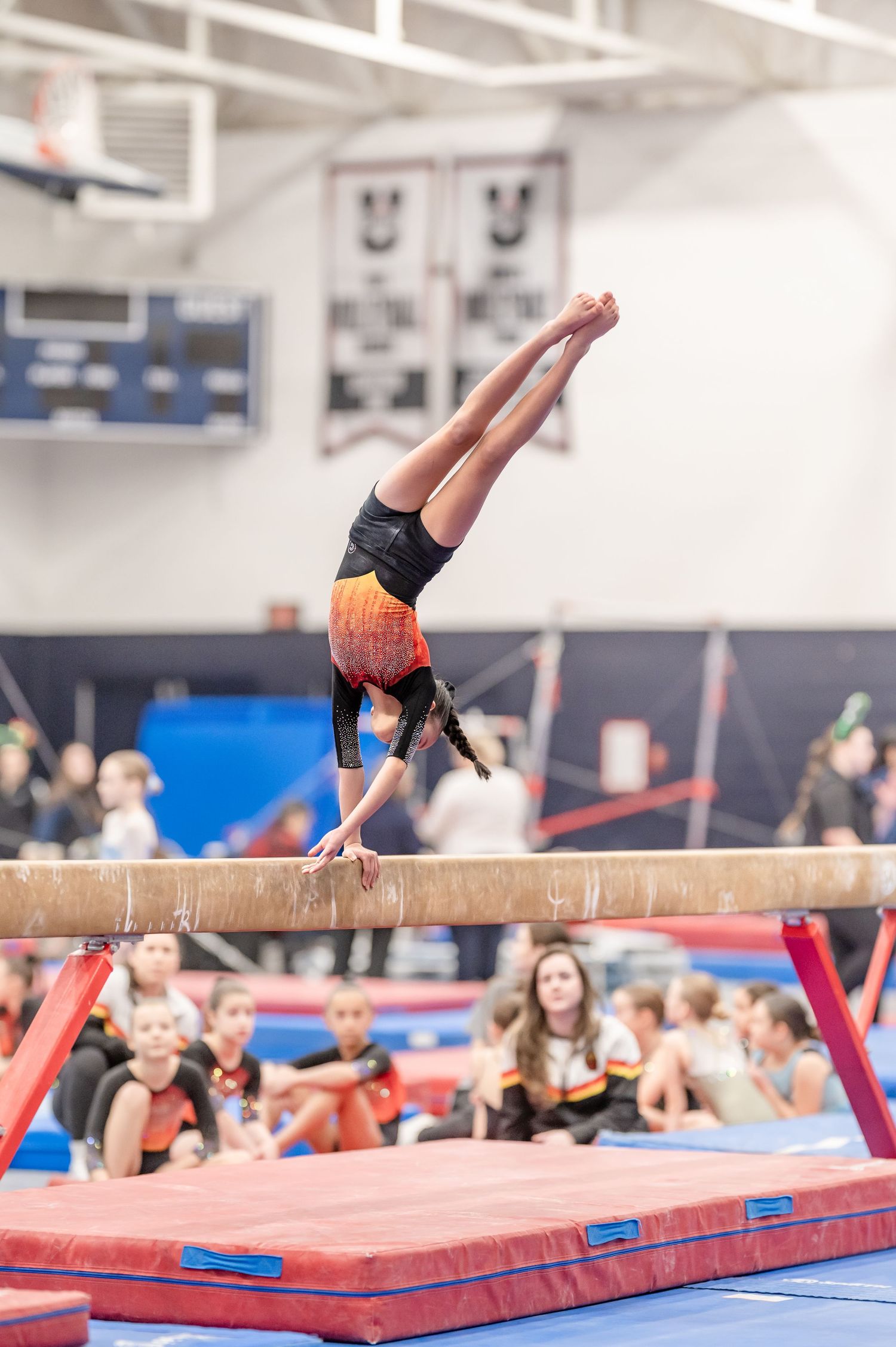Young gymnast performing a handstand on a balance beam during a gymnastics competition.