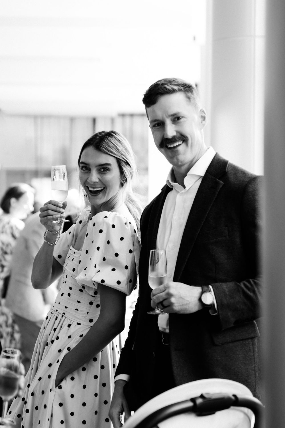 Smiling couple in formal attire toasting with champagne glasses at a stylish black and white event celebration.