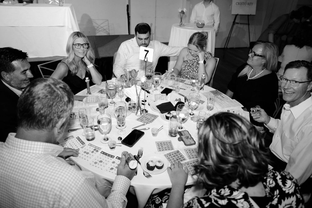 Black and white image of guests in formal attire gathered around a round table at a charity bingo night event.