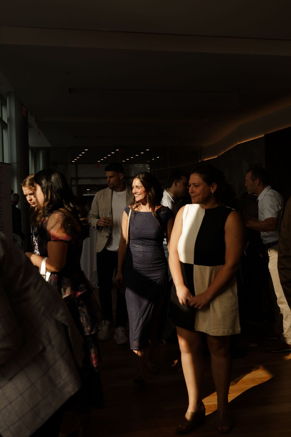 Guests mingling in a dimly lit modern venue hallway during a stylish evening charity or corporate event gathering.