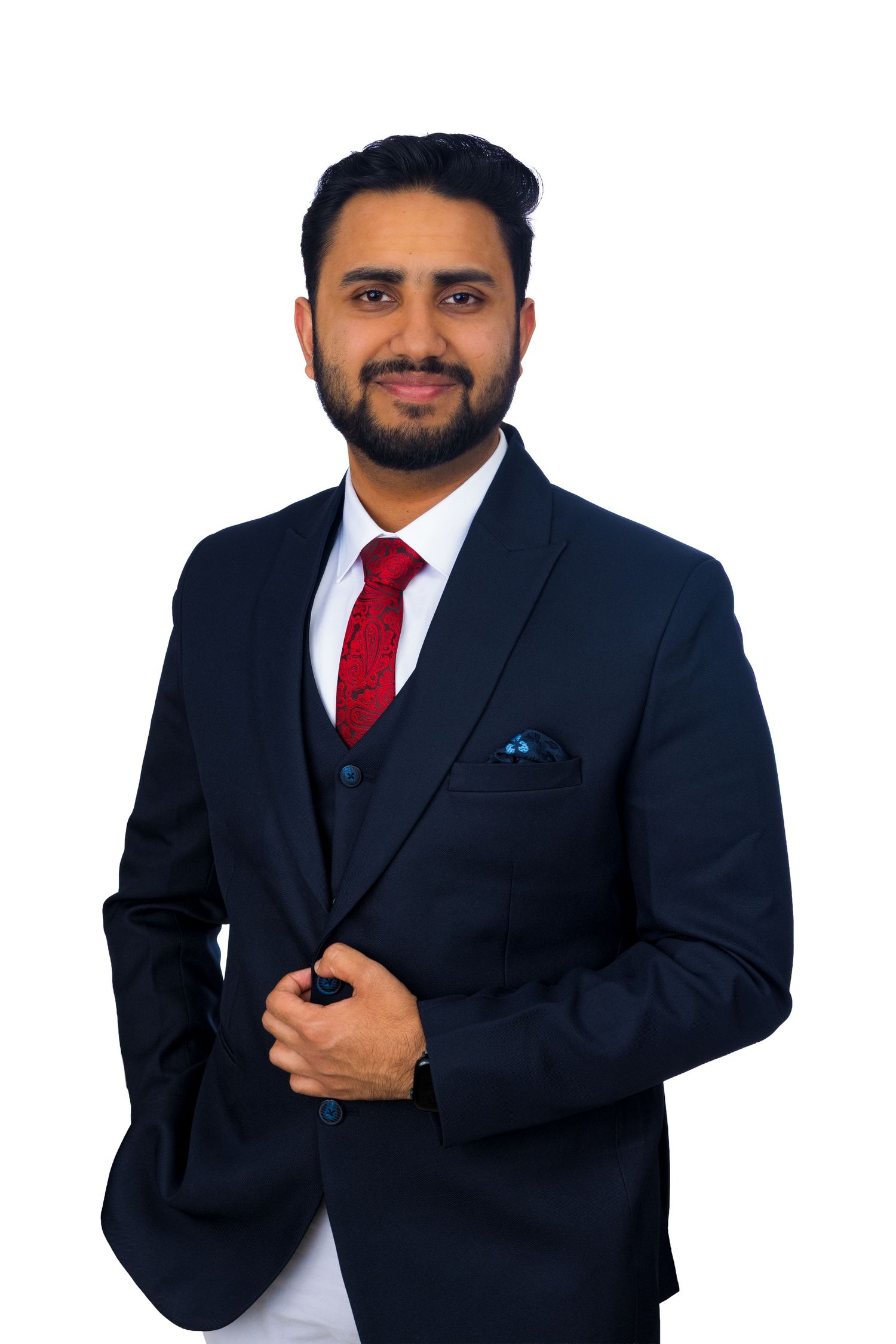 Professional man in navy suit with red tie and pocket square smiling against white background.