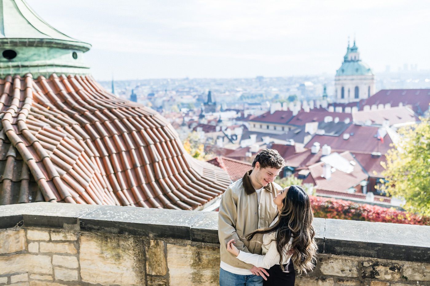Panoramic view of historic Prague cityscape with red-tiled roofs and ornate architecture under bright blue sky.