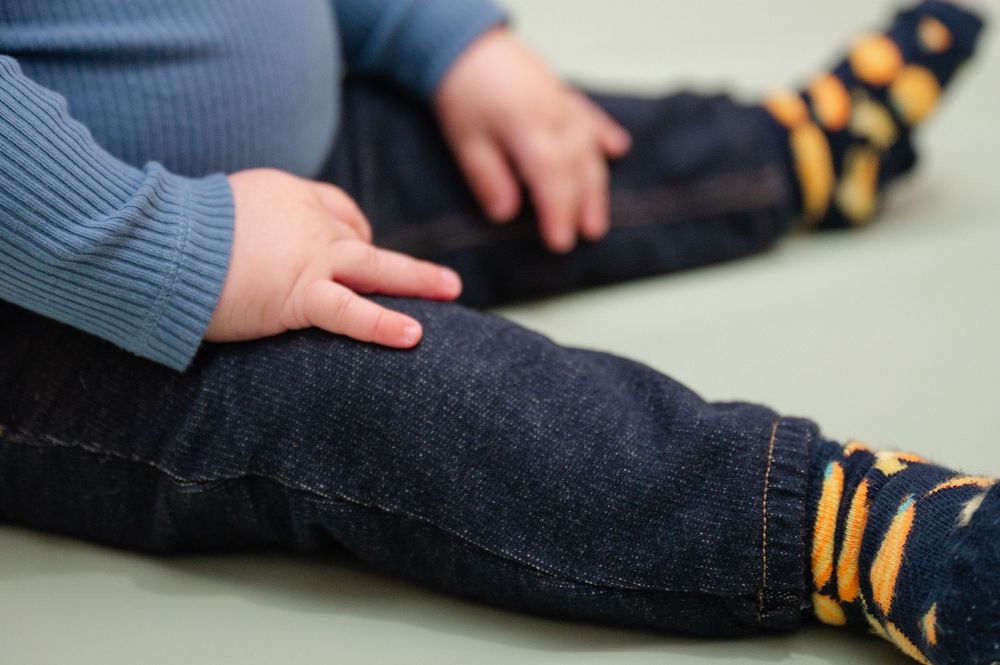 Close-up of a baby's hand resting on an adult's denim-clad leg, both wearing colorful striped socks.
