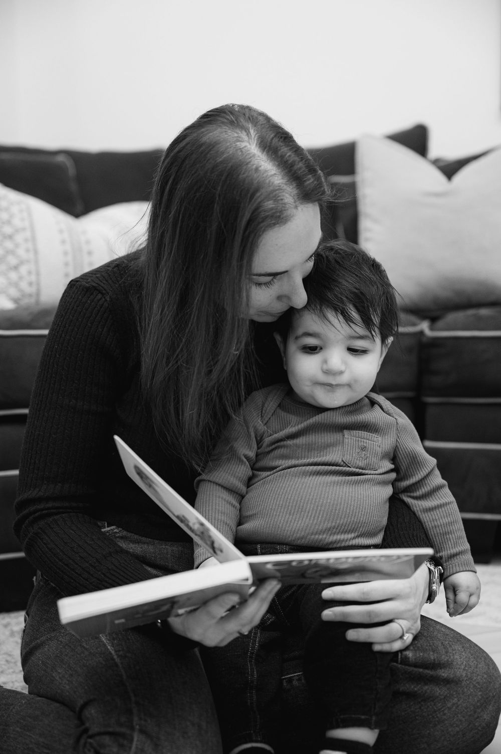 Mother tenderly reading a picture book with her baby boy in a black and white portrait.