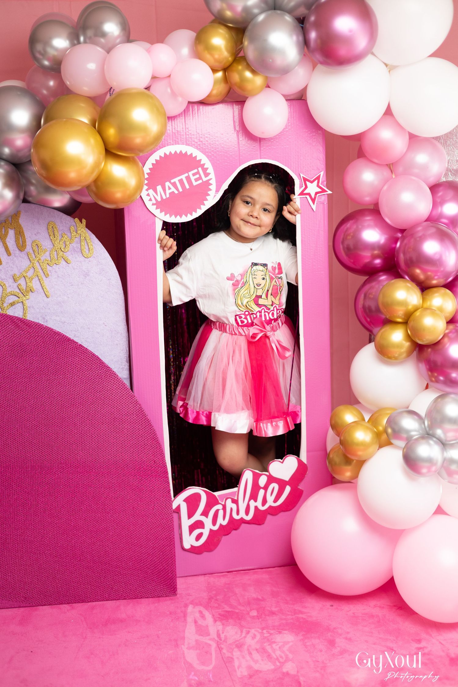 Girl poses in Barbie Mattel box prop at pink balloon birthday party celebration.