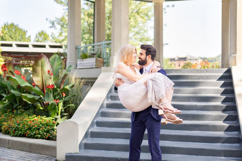 Groom carries bride in his arms on outdoor steps surrounded by lush greenery at a wedding venue. Cincinnati Elopement Photographer