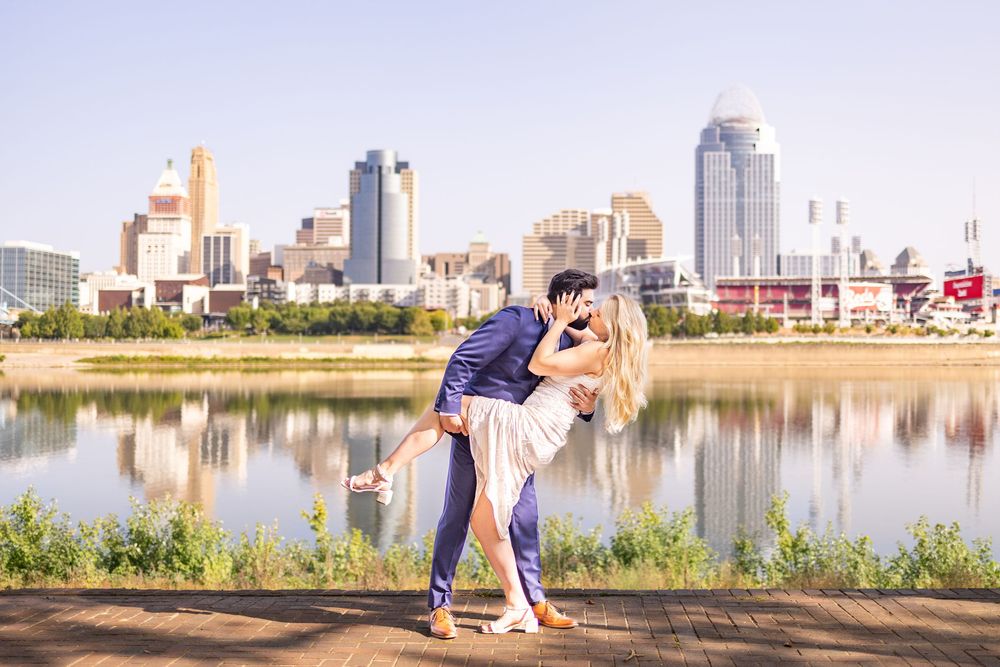 Couple sharing a romantic dip kiss with Cincinnati skyline and Ohio River reflecting in the background.