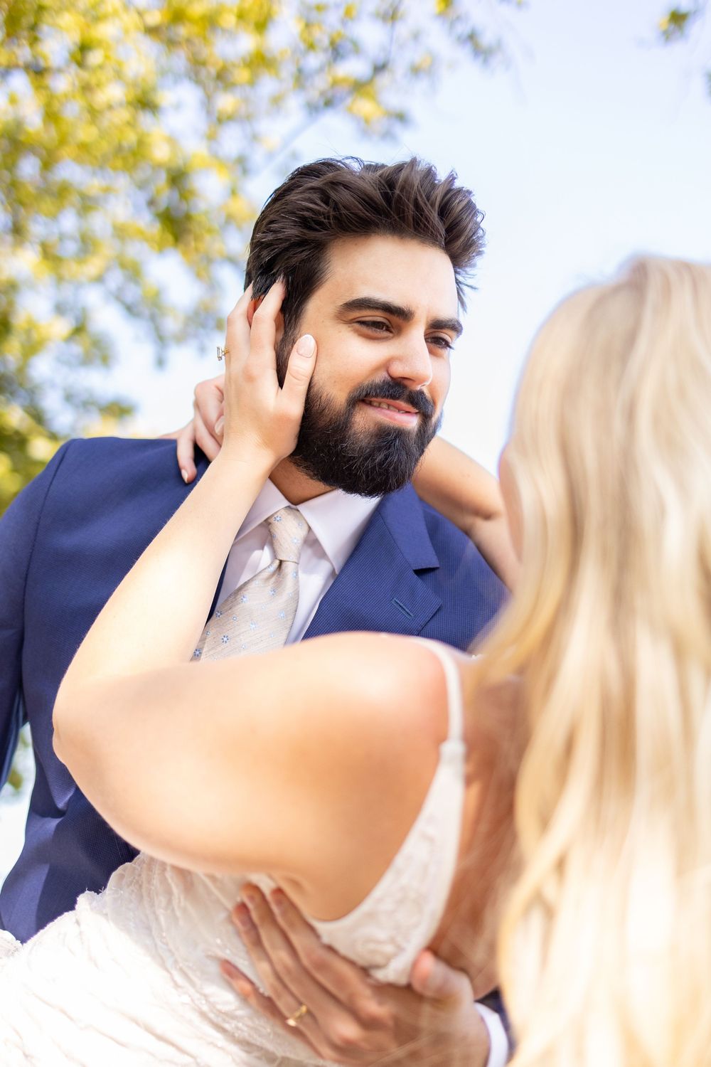 Bride and groom share a romantic moment outdoors, with bride touching groom's face as he smiles in a blue suit. Cincinnati Elopement