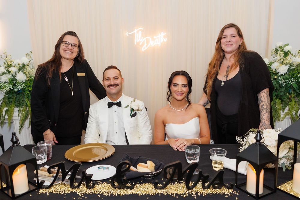 Wedding planners with bride and groom in front of chiffon backdrop featuring neon “Till Death” sign at modern wedding ceremony setup