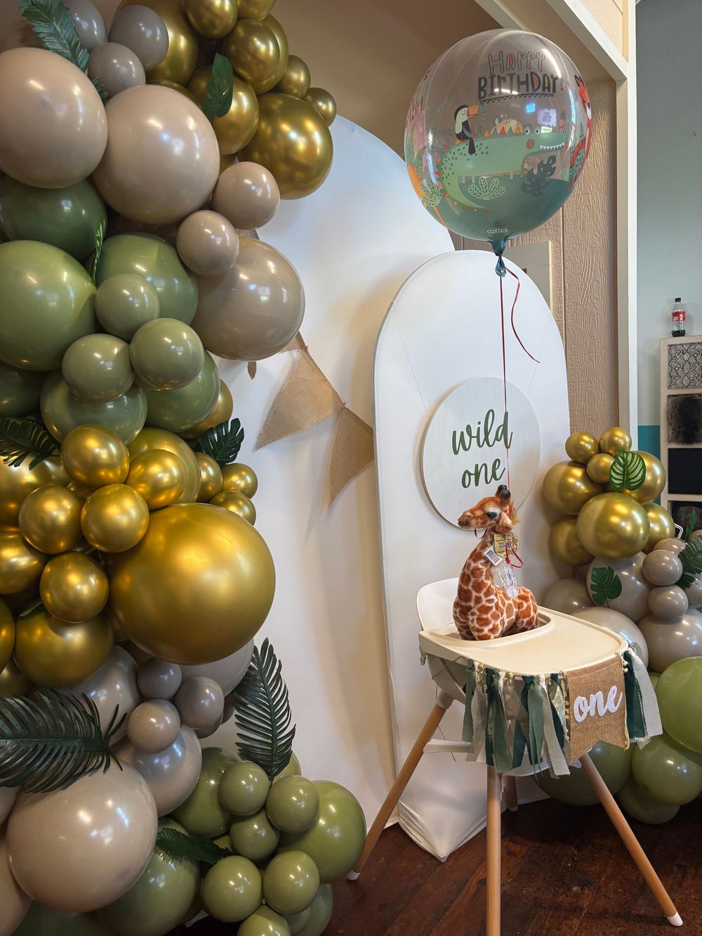 Wild One first birthday party with jungle balloon garland, giraffe stuffed animal, and safari themed decor.