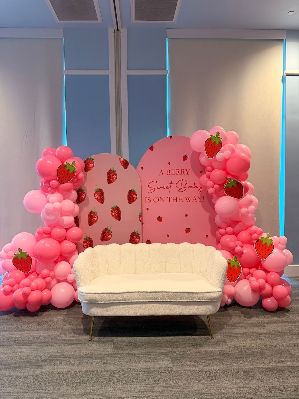 Berry Sweet baby shower with white boucle scalloped loveseat and pink red balloon arch styled for luxury modern celebration décor setup