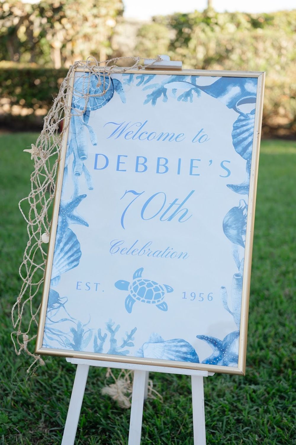 Gold frame welcome sign on white wooden easel displayed at elegant birthday entrance with coastal luxe styling and décor details